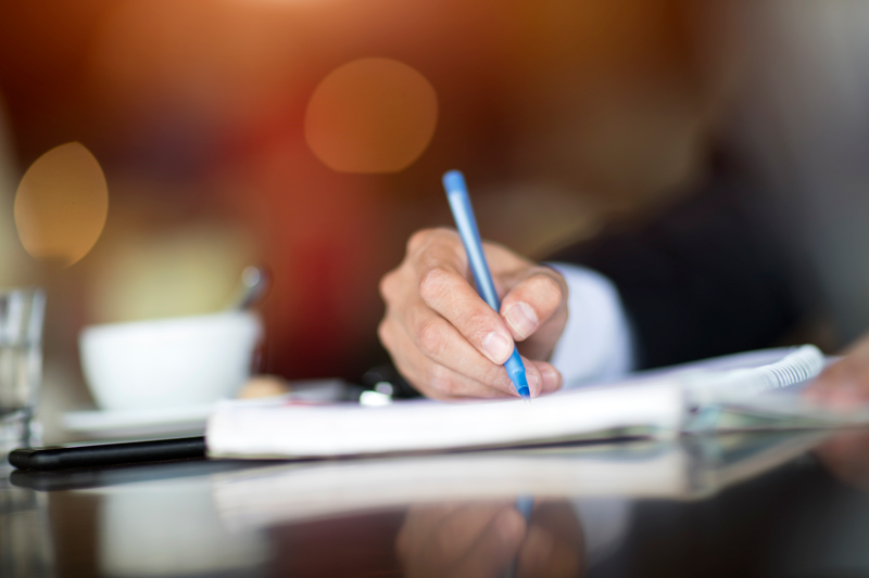 business person writing a letter on paper with a blue pen