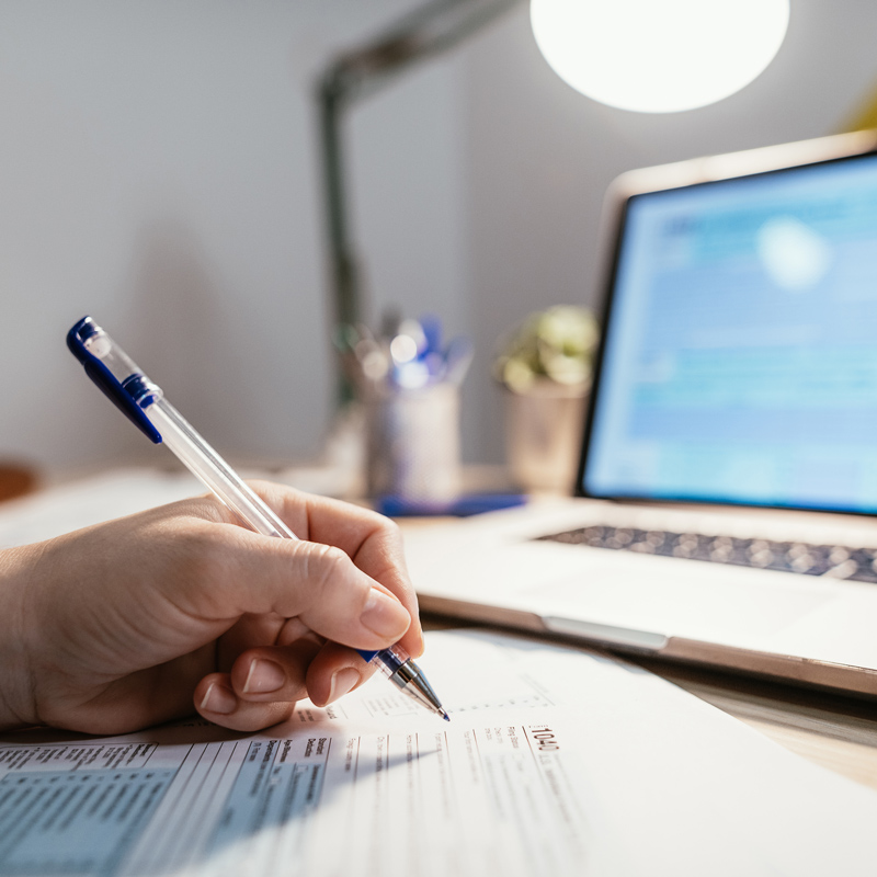 Person filling out tax return form in front of laptop