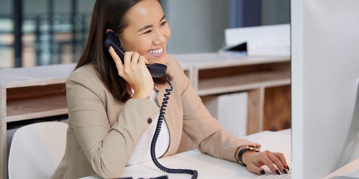Shot of a young woman using a telephone and computer in a modern office va