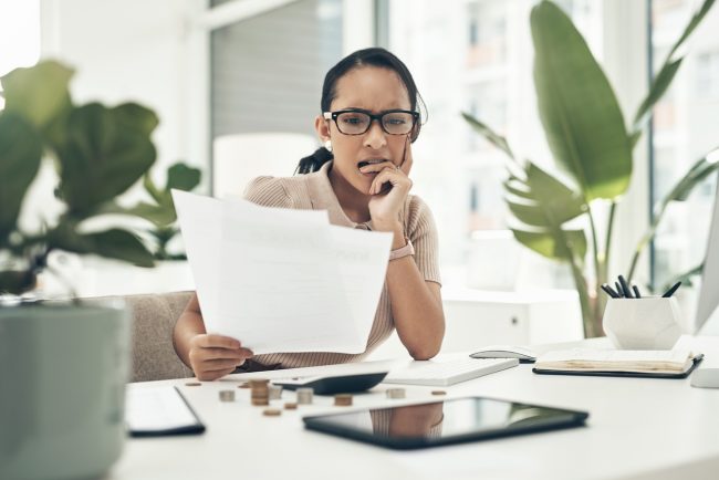 Shot of a young businesswoman looking stressed out while calculating finances in an office errors